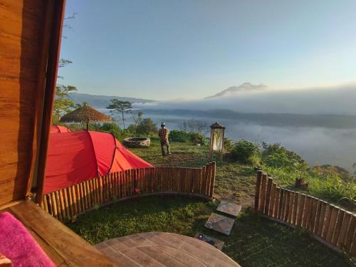 a man standing in front of a tent with a view of a mountain at Kintamani Adventures 'Hide in Nature lodge' in Kintamani