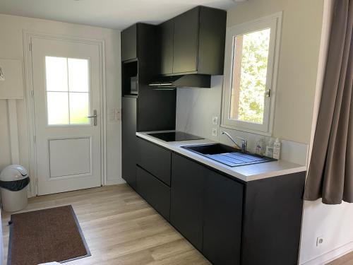 une cuisine noire avec un évier et une fenêtre dans l'établissement Cottage YVEL au Pied du lac au Duc, son Golf et sa Base Nautique, à Ploërmel
