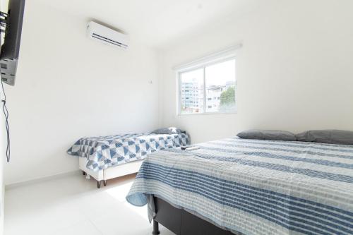 Duas camas num quarto com paredes brancas e uma janela em Pirangi Prime #05 - Triplex Vista Mar em Pirangi do Norte por Carpediem em Parnamirim
