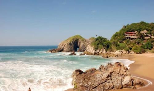 a beach with a large rock in the ocean at Shambhala Visión in Zipolite