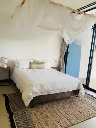a bedroom with a bed with white sheets and a window at Villa Luasah in Vila Praia Do Bilene