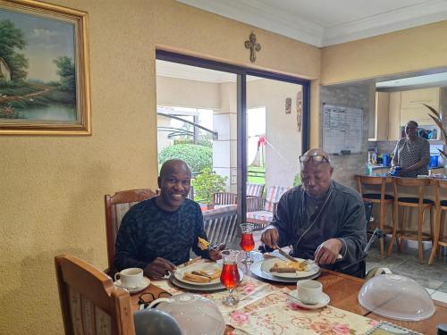 Dois homens sentados à mesa a comer. em Leondale Guest House em Germiston