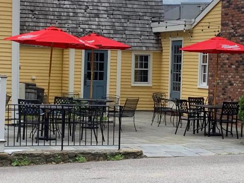 eine Terrasse mit Tischen, Stühlen und roten Sonnenschirmen in der Unterkunft The General Stanton Inn in Charlestown