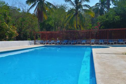 a blue swimming pool with chairs and palm trees at Hotel Arcoiris in Puerto Escondido