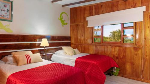 a bedroom with two beds with red sheets and a window at The Wooden House Hotel in Puerto Villamil