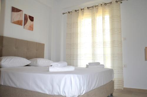 a bedroom with a bed with white sheets and a window at Α & D Perikleous Apartments in Kyllini