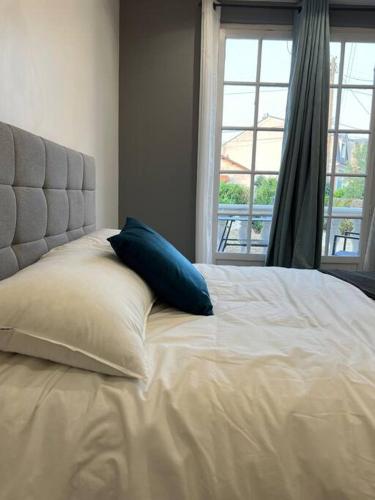 uma cama branca com almofadas azuis e uma janela em Appartement Élégant proche RER/ CDG / Parc des Expos em Sevran