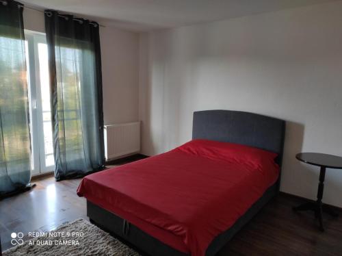 um quarto com uma cama vermelha com uma mesa e janelas em Meri rooms em Bihać