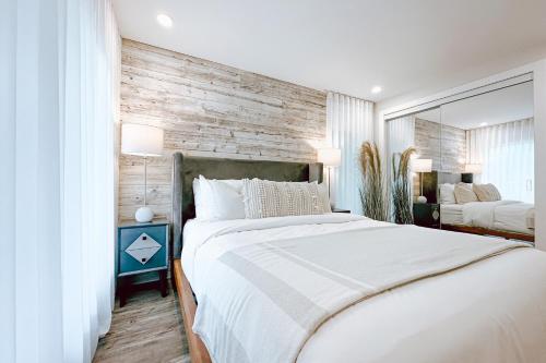 1 dormitorio con cama blanca y pared de madera en Le PanoramiK by Gestion ELITE, en Mont-Tremblant