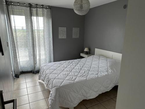 a bedroom with a white bed and a window at La maison du Chêne 2 in Miniac-Morvan