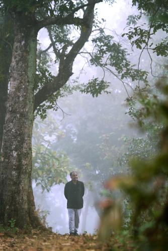 a man standing next to a tree near a river at Whistling Woodzs Resort in Dandeli