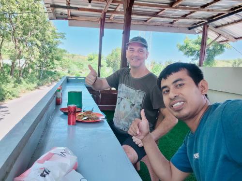 two men sitting at a picnic table giving thumbs up at Satu Hati Homestay in Ekas