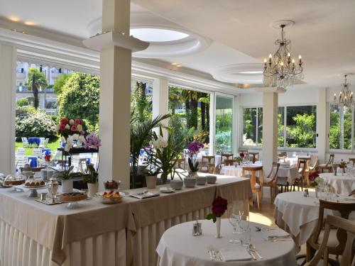 una sala da pranzo con tavoli e sedie bianchi e finestre di Hotel Royal a Stresa