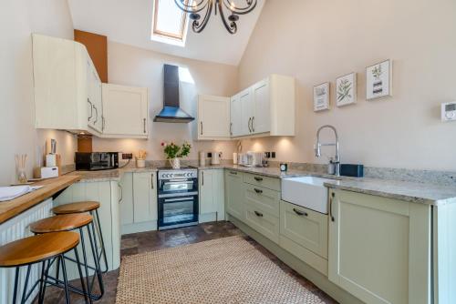 a kitchen with white cabinets and counters and stools at The Old Moat Barn - With Private Hot Tub in Stockton-on-Tees