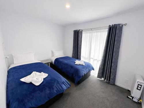 1 dormitorio con 2 camas con sábanas azules y ventana en Brylin Motel, en Rotorua