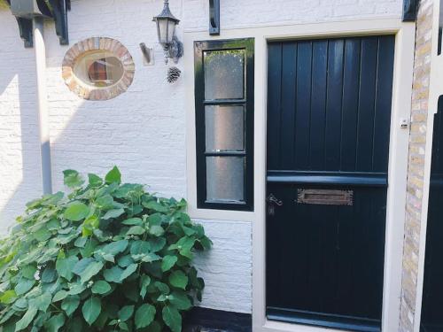 Una porta nera su una casa bianca con un cespuglio di Uniek vakantieverblijf Den Burg a Den Burg