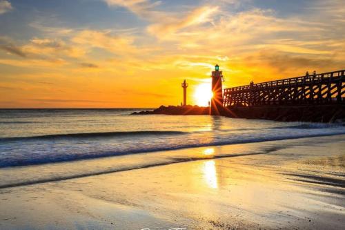 une jetée avec un phare et l'océan au coucher du soleil dans l'établissement Appartement dans résidence calme, à Capbreton