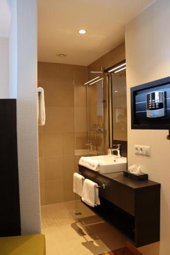 a bathroom with a sink and a tv on a wall at EINSTEIN Hotel am Römerpark in Andernach