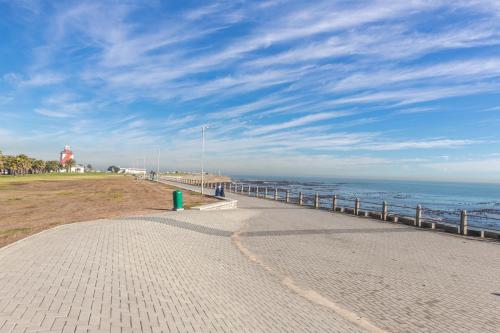 a brick walkway next to the ocean with a pier at Little Gem On The Promenade in Cape Town