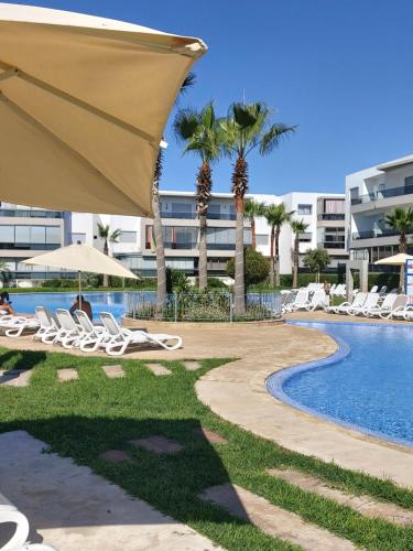 un complejo con piscina, sillas y un edificio en Blanca Beach bel appartement avec wifi et Parking, en Sidi Rahal