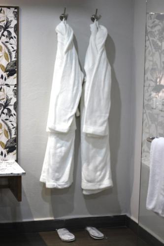 two white robes hanging on a wall in a bathroom at Ecolux Boutique Hotel in Komatipoort