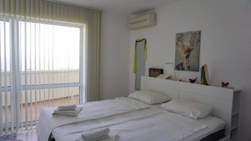 Dormitorio blanco con cama y ventana grande en Апартаменти Сънбрийз - Sunbreeze Apartments, en Byala