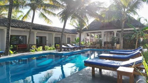 a resort swimming pool with lounge chairs and palm trees at little pompeji boutique hotel - adults only in Jambiani