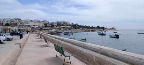 Una fila de sillas colocadas en una acera junto al agua. en The Pines, en Marsaskala
