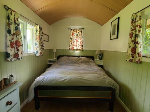 a bed in a small room with two windows at Penn Bergeyn Shepherd's Huts in Exeter