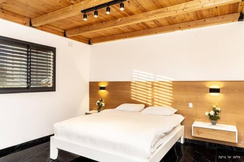 a bedroom with a white bed and a wooden ceiling at מאיורי בוטיק - וילה מקסימה עם בריכה פרטית ונוף מהמם למשפחות בלבד in Mishmār Hāyardin