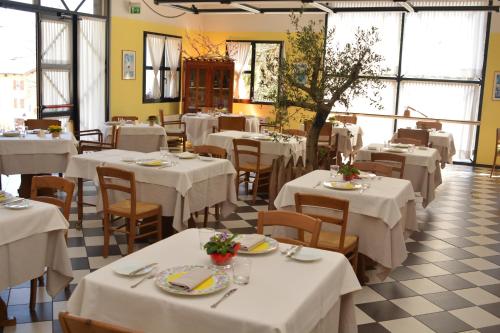 un restaurante con mesas y sillas blancas y ventanas en Hotel Villa Flora, en Roncegno