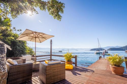 a wooden dock with chairs and an umbrella and the water at Pousada Cruzoé in Praia de Araçatiba