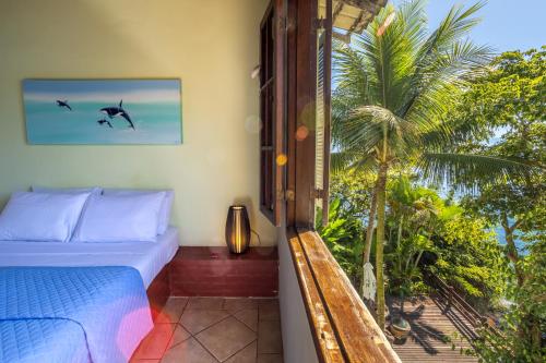 a bedroom with a bed and a window with a palm tree at Pousada Cruzoé in Praia de Araçatiba