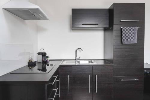 a kitchen with dark wood cabinets and a sink at Les Figuiers - Appartement de Standing avec 2 Chambres in Andenne