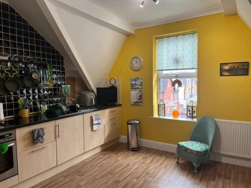 a kitchen with yellow walls and a chair and a window at Cosy & Calm Escape by the Sea in Lytham St Annes
