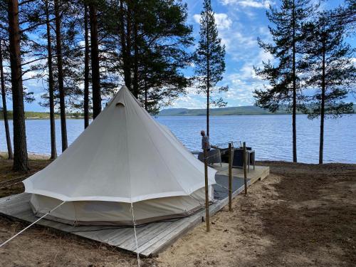 a man standing next to a white tent next to a lake at Osensjøen Camping in Valmen