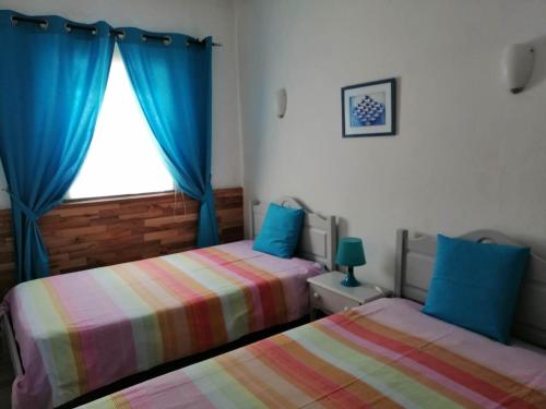 1 dormitorio con 2 camas y una ventana con cortinas azules en Moradia com piscina na Lagoa de Albufeira, en Sesimbra