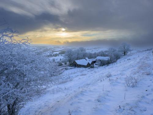 a snow covered field with a house on a hill at The Barn at Hill House in Buxton