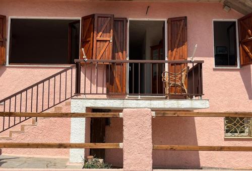 Edificio rosa con balcón con puertas de madera en Il Maestrale en Isola Rossa