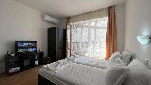a bedroom with a bed and a tv and a window at Bratanov Royal Palm Apartments in Sveti Vlas