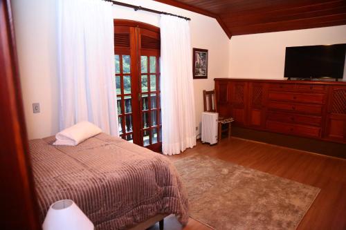 a bedroom with a bed and a tv and a window at Pousada Miraflores in Campos do Jordão