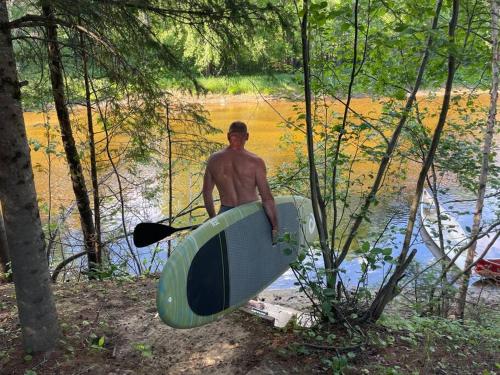 a man holding a surfboard next to a body of water at Chalet NABU L'Ours - Rivière - Billard in Saint-Alexis-des-Monts