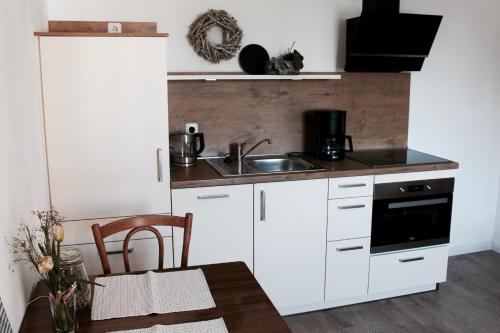 cocina con armarios blancos, fregadero y mesa en Landhaus Weserbergland - Elsa, en Vahlbruch