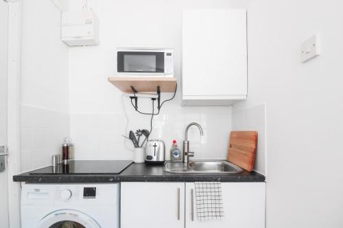 a white kitchen with a sink and a microwave at Lovely Studio Flats in Hackney in London