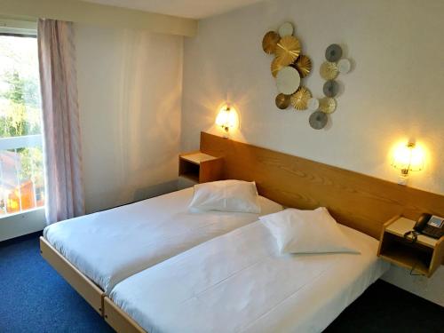 una habitación de hotel con una gran cama blanca y una ventana en Hôtel de la Plage à Gland, en Gland