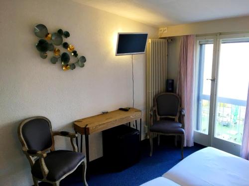 a room with a desk and two chairs and a television at Hôtel de la Plage à Gland in Gland