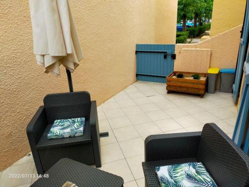 een patio met 2 stoelen, een tafel en een parasol bij Appartement en résidence avec parking in Le Barcarès