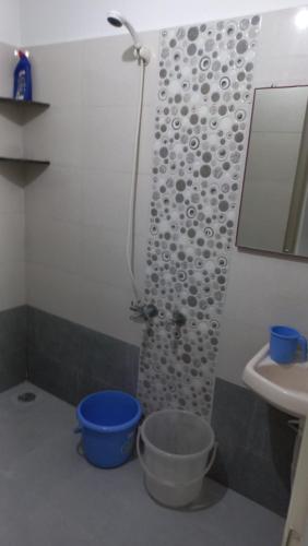 a bathroom with a shower and a blue bucket at The Nest - Harmony Inn in Sangli