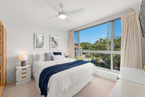 a white bedroom with a bed and a large window at Shoal Bay Shores, modern beachfront unit + Wifi in Nelson Bay