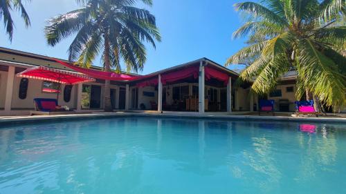 a large swimming pool in front of a house with palm trees at Villa Les Cocotiers in Nosy Be